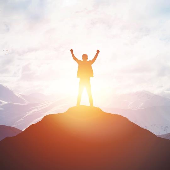 Silhouette of someone standing on a mountaintop with their hands over their head