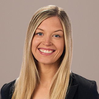 Woman with long blonde hair and a black blazer smiles on a white background