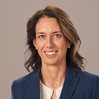 Brunette woman in a navy blue blazer smiles on a white background