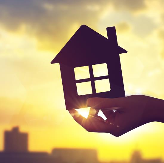 Someone holds a 2-D model of a house with the sun shining through it