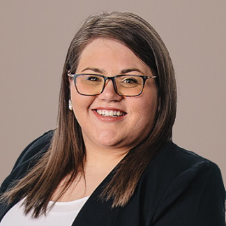 Brunette woman in glasses and a black blazer smiles on a white background