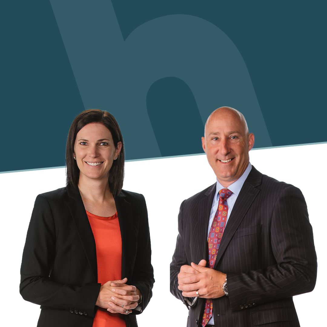 Man and woman in business clothes smile in front of a split white and dark blue background with the lowercase h logo