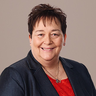 Woman with short dark hair and a black blazer smiles on a white background