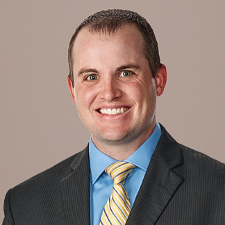 Dark haired man in a black striped blazer smiles on a white background
