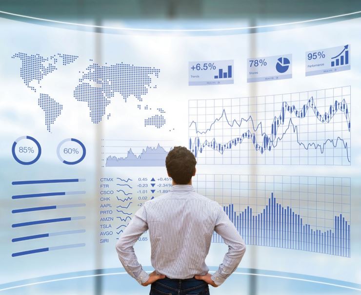 Shot from the back, a man stands with hands on hips and looks at a digital wall of charts and graphs