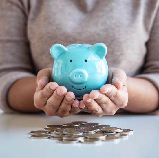 A close up of someone holding a blue ceramic piggy bank above a pile of silver dollars
