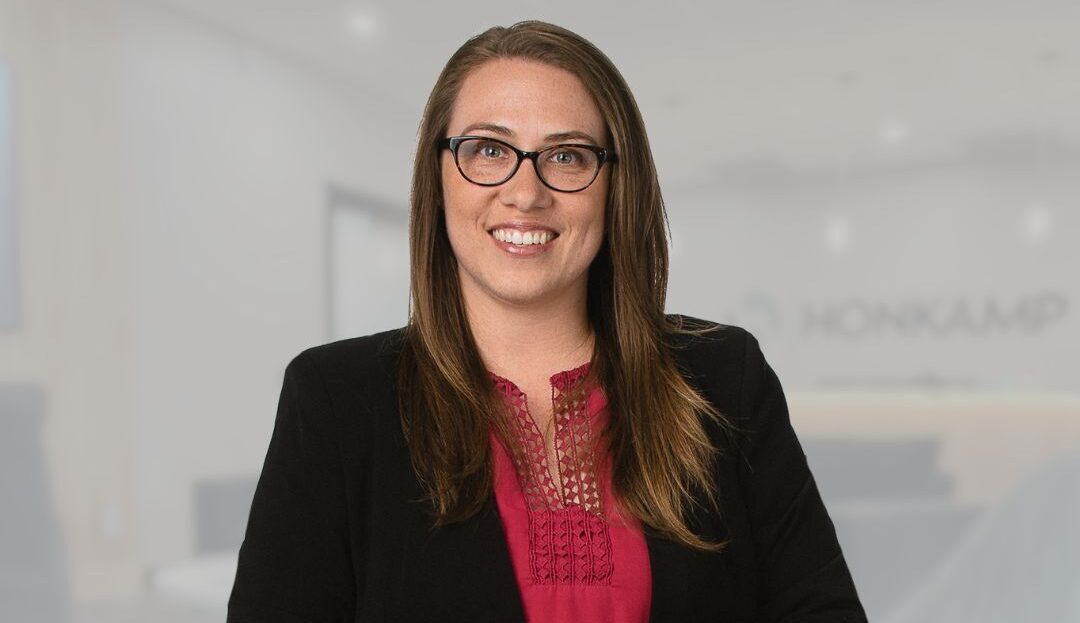 Brunette woman in glasses and a black blazer smiles in a Honkamp lobby with a pale overlay