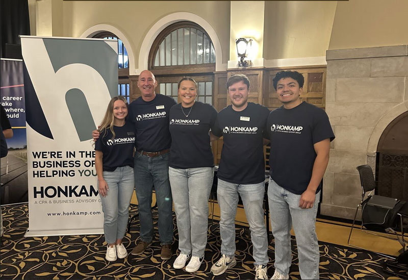 Three men and two women in matching Honkamp tshirts pose together in an event space