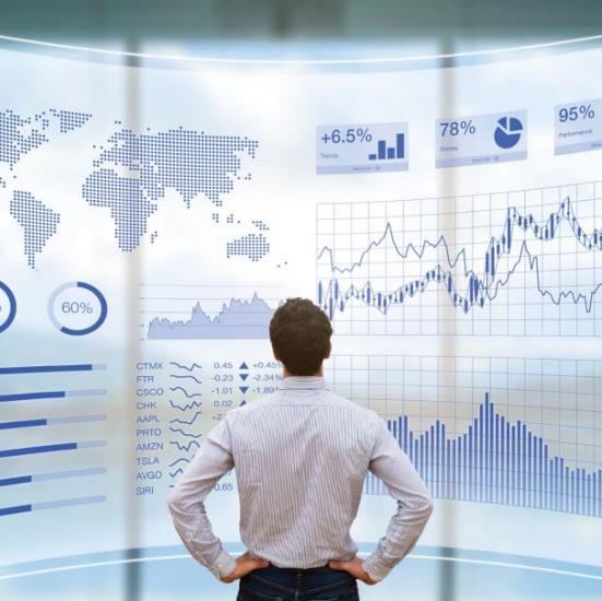 Shot from the back, a man stands with hands on hips and looks at a digital wall of charts and graphs