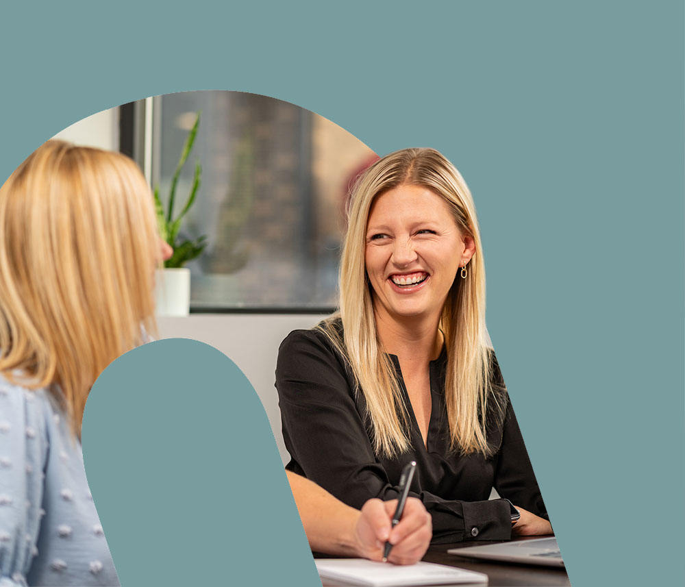 In a cutout of the Honkamp logo, two blonde women laugh together in a conference room