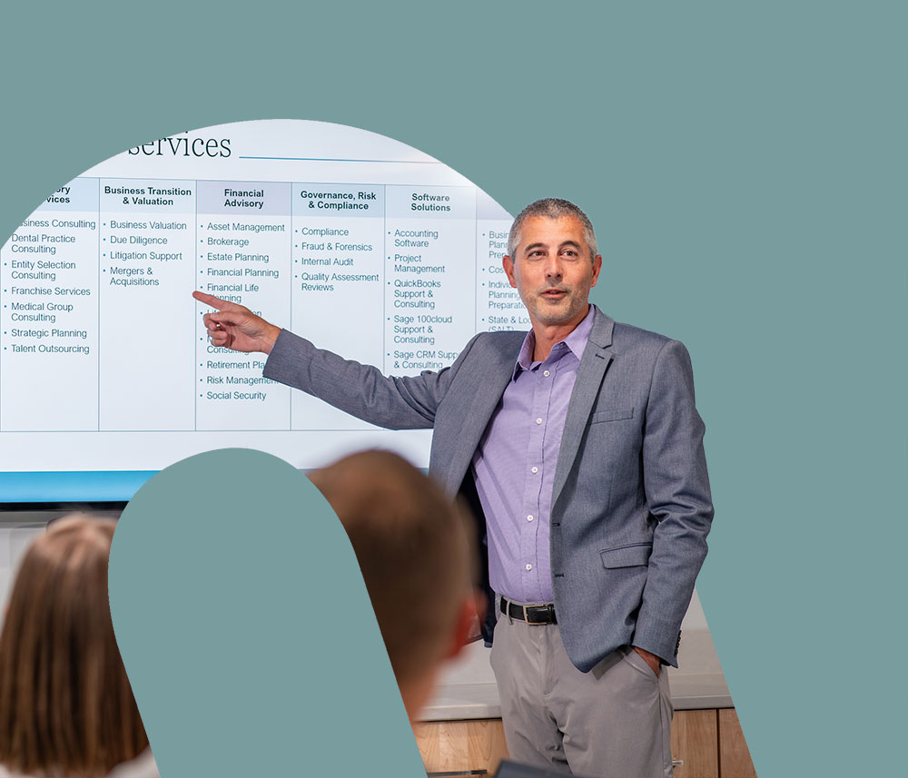 In a cut out of the Honkamp logo, a man in a blazer points to charts on a large screen