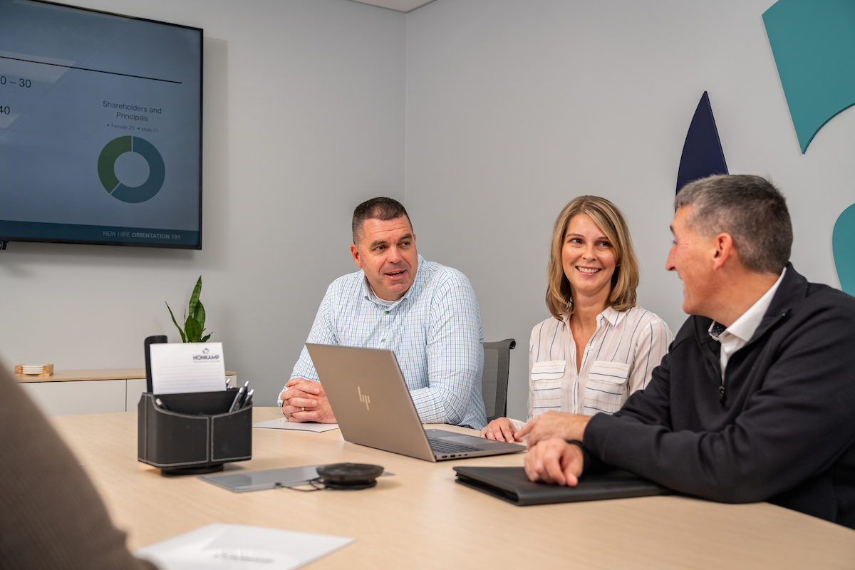 Two men and a woman sit and talk together in a Honkamp conference room