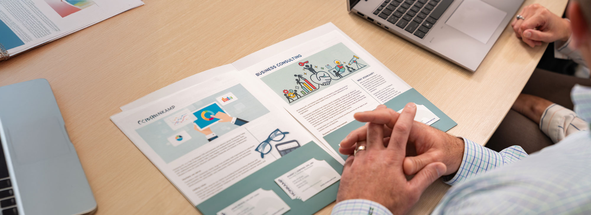 Colorful one-pagers describing services appear in a green folder on a wooden table