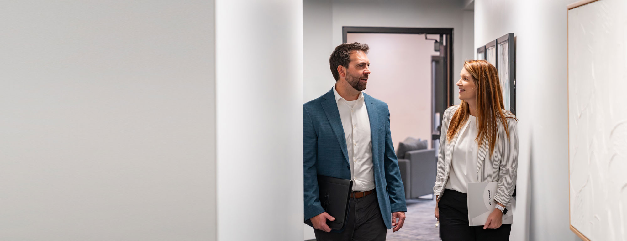 Man and woman in business clothes walk and talk in a bright hallway