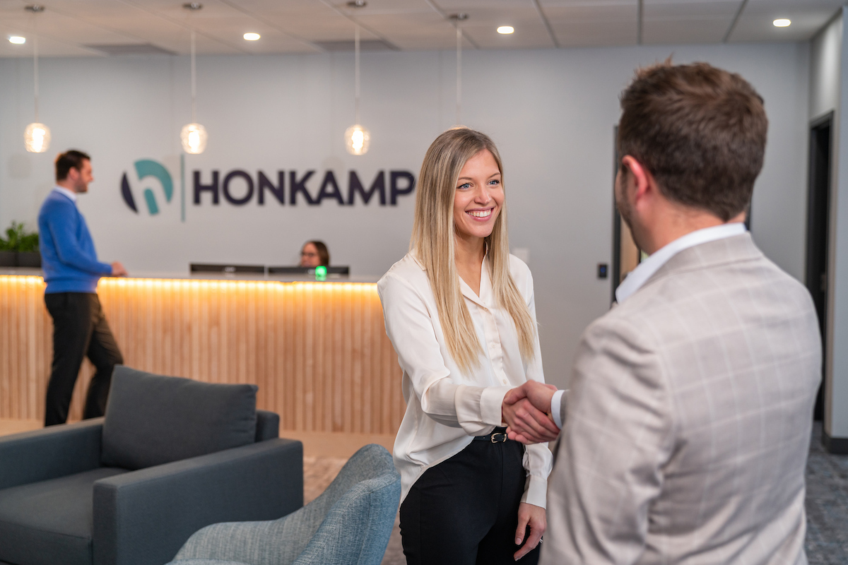 In a Honkamp lobby, a blonde woman shakes hands with a man with his back to the camera