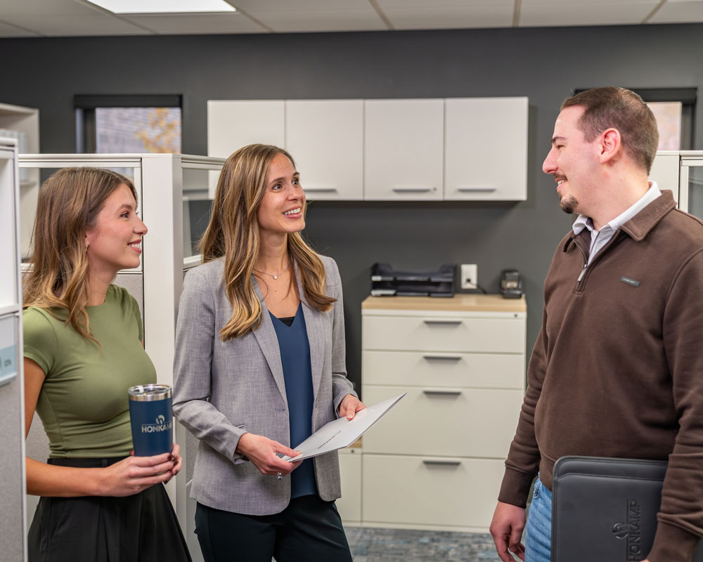 Two women and a man smile and talk in an office