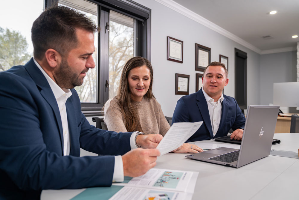 A woman sits between two men in a bright conference room, reviewing papers