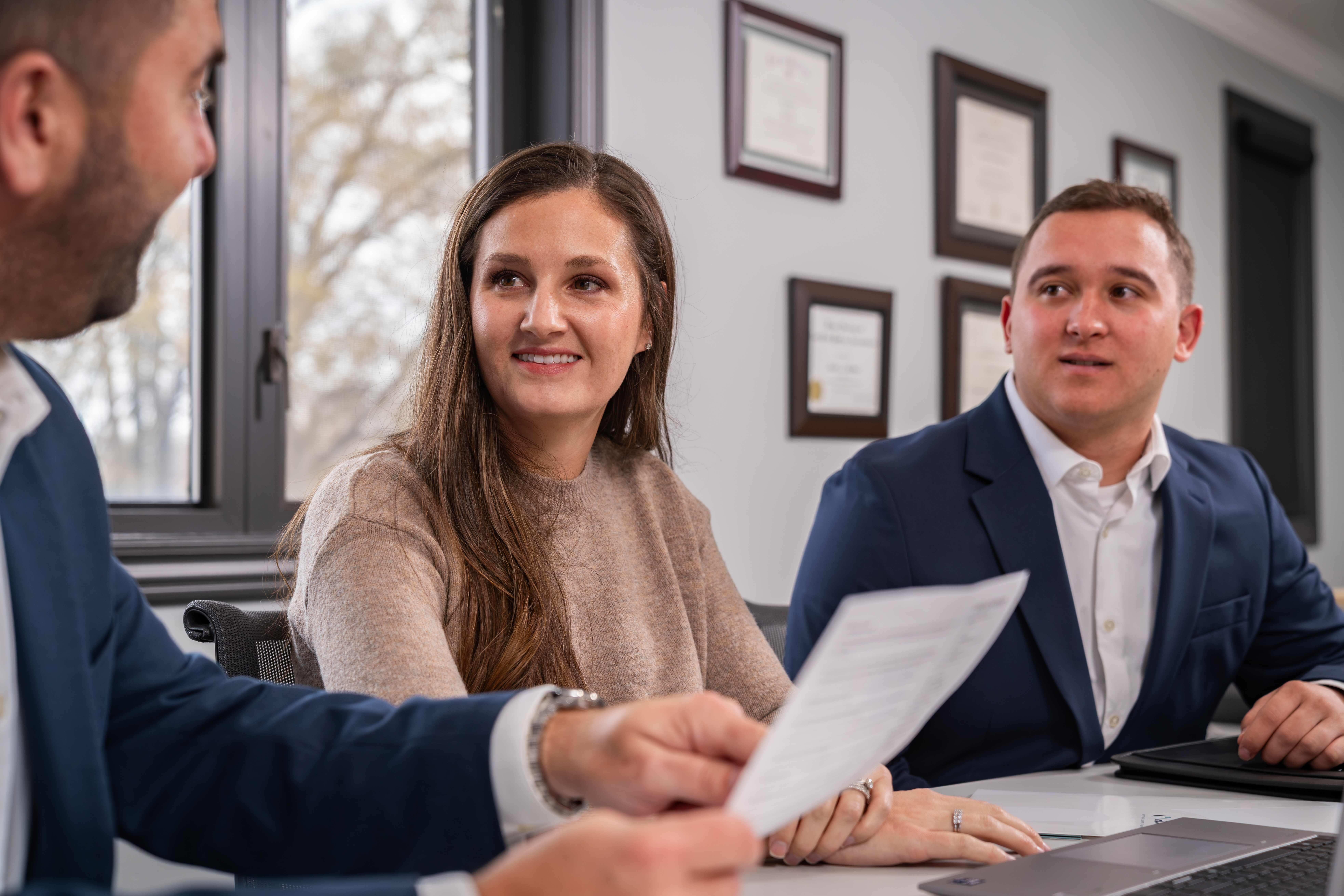 Man and woman sit in a conference room and speak to another man slightly blurred in foreground