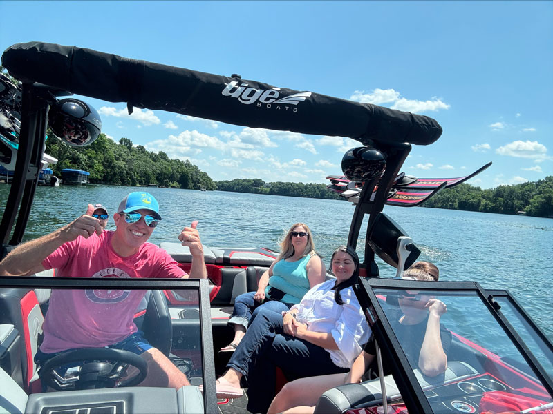 Group of men and women smile together while riding on a boat across a scenic river