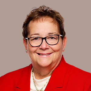 woman in red blazer smiles on a tan background